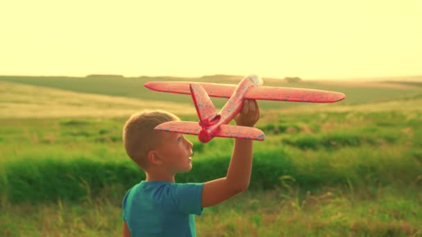 O rapaz quer tornar-se astronauta piloto. Movimento lento. Menino adolescente feliz brinca com avião de brinquedo no campo ao pôr do sol. As crianças brincam com avião de brinquedo. Sonhos adolescentes de voar, tornar-se piloto. Voo de avião — Vídeo de Stock