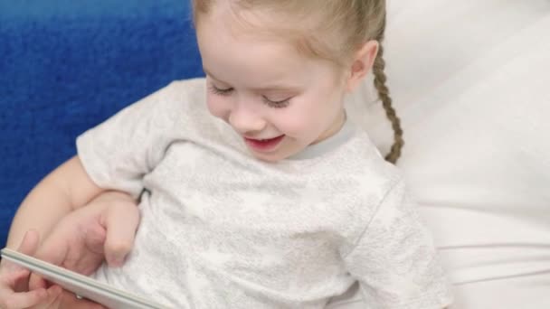 Menina, criança sorri, segurando tablet para jogar na Internet, brincando junto com o pai em casa. Família feliz. Filha bonito, criança e pai usam tablet digital enquanto deitado no sofá. Família em casa. — Vídeo de Stock