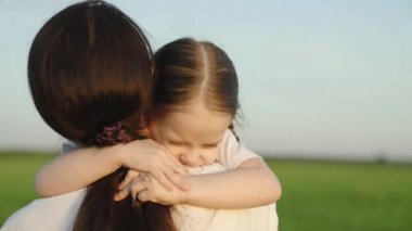 Küçük kızım, çocuk ilkbaharda parkta annesine sarılıyor. Çocuk gülümsüyor, kameraya bakıyor. Anne, çocuk yaz parkında sarılıyor. Mutlu çocuk ailesi, anne yaz parkında kızına sarılıyor. Çocuk, anne.