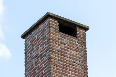 Üst kısmın izole edilmiş bir portresi uzun bir duvar ustası kırmızı tuğla baca bir evin siyah kiremit çatısında gündüz vakti mavi bir gökyüzü ve bazı bulutlar.