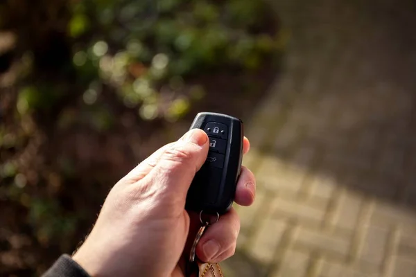 車の鍵を持っている人の手のクローズアップ肖像画は タムでロック解除ボタンを押してください リモコンにはロック解除 ロック トランクアイコンが付いています ストック画像