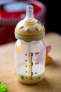 Tahta bir tahtanın üzerinde duran süt dolu bir bebek şişesinin yakın plan portresi. Cam hemşirelik şişesinde hala bir formül var ve plastik meme ucu ya da şişe memesi var.. 