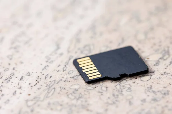 A close up portrait of the back of a black micro SD card lying on a stone surface, the connectors of the small piece of storage electronics hardware is visible.
