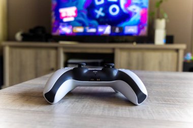 BRECHT, BELGIUM  AUGUST 14 2022 A back portrait of a Sony Playstation 5 wireless controller on a wooden table in front of a television showing the PS5 playstation plus screen in a living room.
