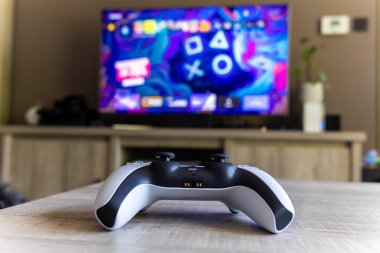 BRECHT, BELGIUM  AUGUST 14 2022 Portrait from the back of a Sony Playstation 5 wireless controller on a wooden table in front of a television showing the PS5 playstation plus screen indoors.
