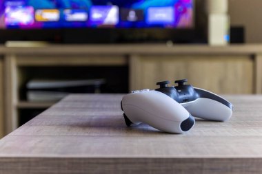BRECHT, BELGIUM  AUGUST 14 2022 A side portrait of a Sony Playstation 5 wireless controller on a wooden table in front of a television showing the PS5 playstation plus screen indoors.