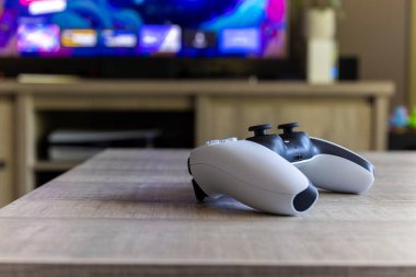 BRECHT BELGIUM  AUGUST 14 2022 A side portrait of a Sony Playstation 5 wireless controller on a wooden table in front of a television showing the PS5 playstation plus screen in a living room.