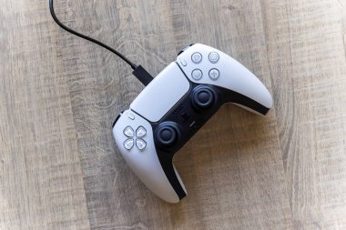 BRECHT, BELGIUM  AUGUST 14 2022 A top down portrait of a white basic playstation 5 controller which is charging with the official USB-C cable. The ps5 device is lying on a wooden table.