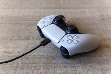 BRECHT, BELGIUM  AUGUST 14 2022 A portrait of a white basic playstation 5 controller which is charging with the official USB-C cable. The ps5 device is lying on a wooden table.