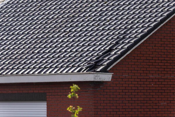 A portrait of a destroyed black tile roof of a house. The building got damaged by a big storm with high wind speeds on the beaufort scale in Belgium due to climate change.
