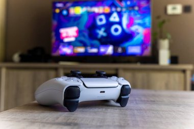BRECHT, BELGIUM 14 AĞUSTOS 2022 Bir Sony Playstation 5 kablosuz kontrolörünün yakın bir portresi Bir televizyon önünde bir oturma odasında PS5 playstation artı ekran gösteren.