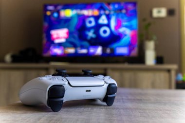 BRECHT, BELGIUM 14 AĞUSTOS 2022 Bir Sony Playstation 5 kablosuz kontrolörünün yakın bir portresi Bir televizyon önünde bir oturma odasında PS5 playstation artı ekran gösteren.