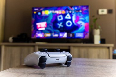 BRECHT, BELGIUM 14 AĞUSTOS 2022 Bir Sony Playstation 5 kablosuz kontrolörünün yakın bir portresi Bir televizyon önünde bir oturma odasında PS5 playstation artı ekran gösteren.