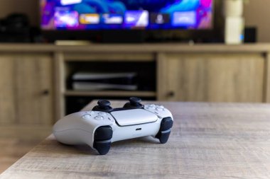 BRECHT, BELGIUM 14 AĞUSTOS 2022 Bir Sony Playstation 5 kablosuz kontrolörünün yakın bir portresi Bir televizyon önünde bir oturma odasında PS5 playstation artı ekran gösteren.