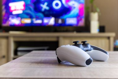 BRECHT, BELGIUM 14 AĞUSTOS 2022 Bir Sony Playstation 5 kablosuz kontrolörünün yakın bir portresi Bir televizyon önünde bir oturma odasında PS5 playstation artı ekran gösteren.
