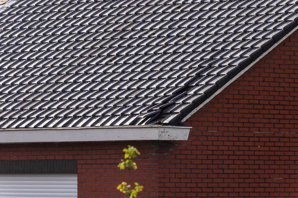 A close up portrait of a destroyed black tile roof of a house. The building got damaged by a big storm with high wind speeds on the beaufort scale in Belgium due to climate change.