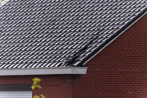A close up portrait of a damaged black tile roof of a house. The building got destroyed by a big storm with high wind speeds on the beaufort scale in Belgium due to climate change.