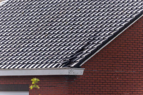 A portrait of a damaged black tile roof of a house. The building got destroyed by a big storm with high wind speeds on the beaufort scale in Belgium due to climate change.