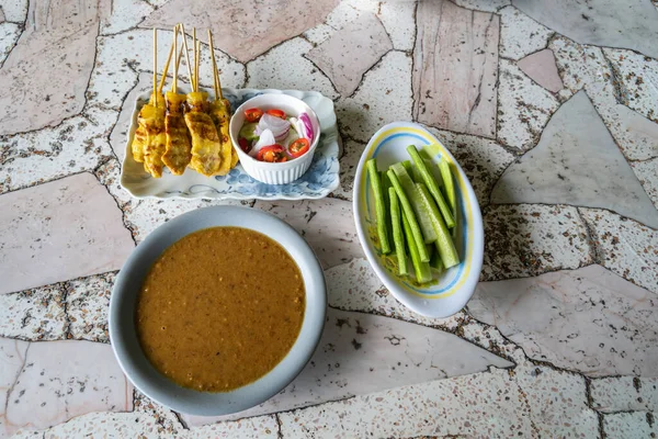 Pork satay şiş, sebzeli bir tabakta ve yanında bir sos..