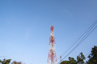 Kırmızı ve beyaz sinyal kuleleri, ağaç tepelerinin üstünde ve elektrik kabloları var..