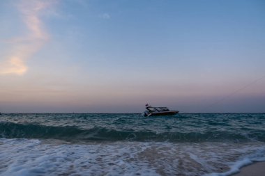 Tekne gün batımından sonra sahilde yüzer, küçük dalgaları görür.