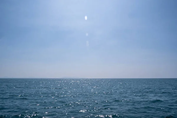 Bulutların görülebildiği bir gökyüzü. Aşağıda deniz var ve güneş ışığını yansıtıyor..