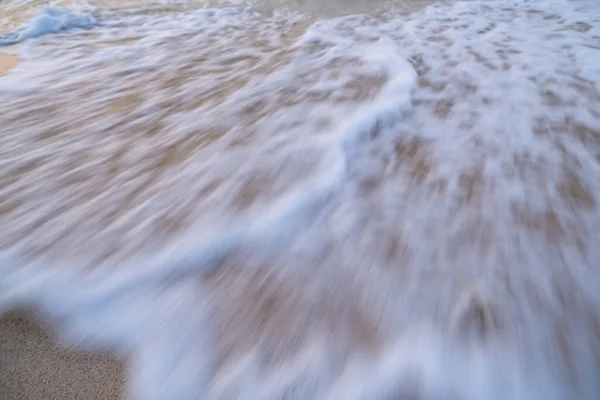 Deniz dalgaları kuma çarpar ve bulanık beyaz bir köpük oluşturur..
