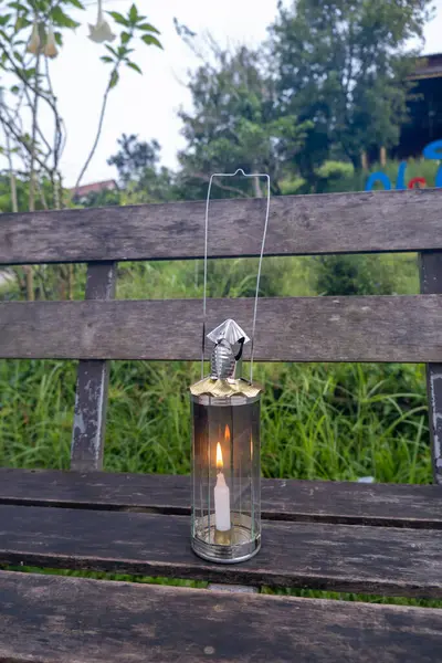 Yanan Birmanya fenerleri ahşap tahtalara konur. Arkalarında çimenlik bir orman vardır..