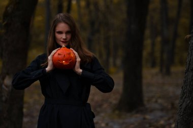 Genç, sıska bir kadının portresi. Ormanda parlayan bir balkabağı tutuyor.