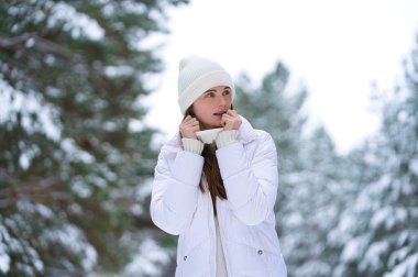 Süveter ve örgü şapkalı mutlu bir kız. Kış anlarının tadını çıkarıyor. Karlı bir sabahta odunun bulanık arka planında eğleniyor.