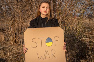 Üzgün kız, Rusya ve Ukrayna arasındaki savaşı protesto eden pankartı tutuyor. Kadın, savaşı durdurmak istiyor. Protesto eylemi. Ukrayna 'daki savaşı durdurun. Ukrayna 'da barış kavramı. Seçici odak