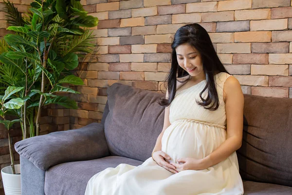 Feliz asiático embarazada mujer en sofá —  Fotos de Stock