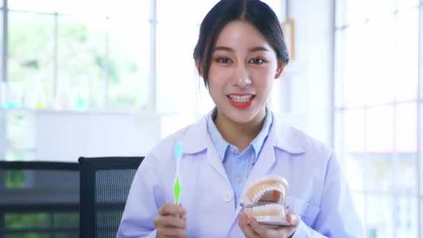 Asiatisk kvinnlig tandläkare visar rätt sätt att borsta tänder hålla mun modell och tandborste — Stockvideo