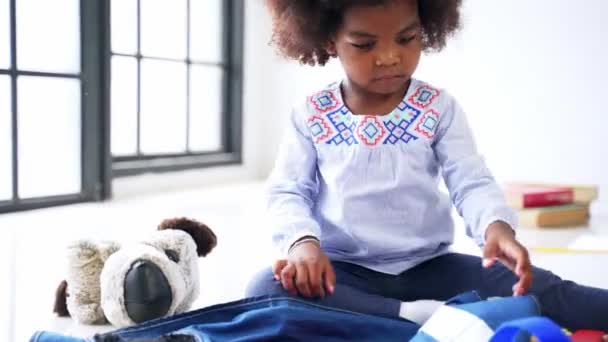 Linda niña afroamericana en ropa casual jugando con una ropa en la habitación en casa — Vídeos de Stock