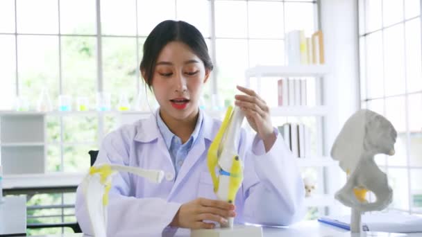 Young Asian woman doctor in labcoat preparing a bone model to describe symptoms from camera pov — Stock Video