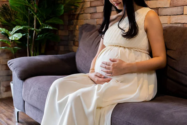 Mujer embarazada tocando al bebé dentro del estómago en el sofá —  Fotos de Stock