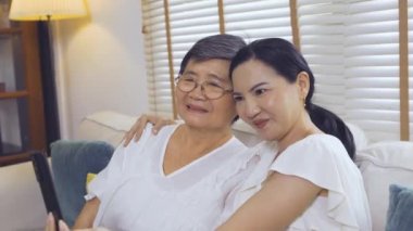 Asyalı anne ve kızı kanepeye selfie çekiyor.