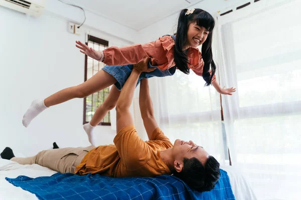 Boldog Ázsiai Apa Fekszik Ágyon Felemeli Lánya Karját Miközben Játszanak — Stock Fotó