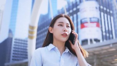 Güzel ve gülümseyen Asyalı bir kadının portresi. Günlük kıyafetler içinde. Şehir caddesinde yürürken arkadaşlarıyla akıllı telefondan konuşuyor.