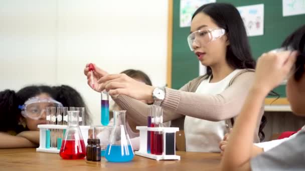 若い女性は 化学について学び 多民族の子供たちと試験管内の液体を混合します アジアの学校教師と科学クラスの学生 — ストック動画