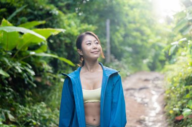 Genç bayan kaşif orman dağ yolunda gülümsüyor ve yürüyüş yapıyor. Dışarıda yürüyen Asyalı kadın..