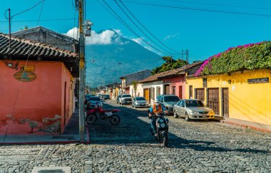 Antigua, Guatemala - 25 Eylül 2021 - Arka planda Agua Volkanı olan motosiklet ve koloni renkli evlerin sokak fotoğrafları