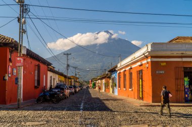 Antigua, Guatemala - 27 Eylül 2021 - arka planda Agua Volcano ile koloni renkli evlerin yanında yürüyen adamın sokak fotoğrafı