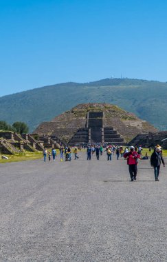Teotihuacan, Meksika - 26 Ağustos 2021 - Arka planda Ay Piramidi ile Ölüler Bulvarı 'nda yürüyen turistlerin dikey görüntüsü