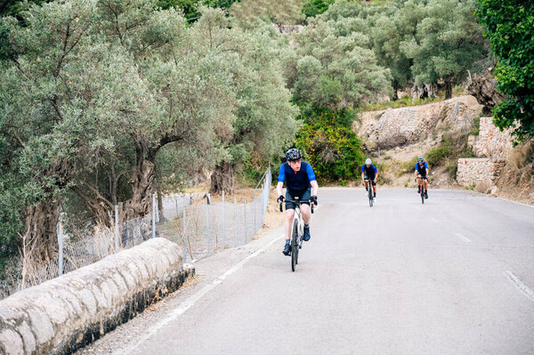 Старший велогонщик с двумя неузнаваемыми велосипедистами на заднем плане на горном перевале