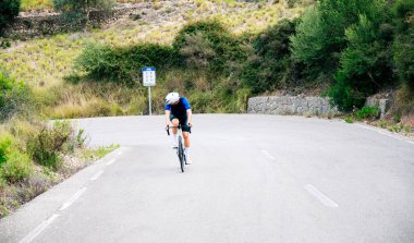 Bir dağ yolunda tepeye tırmanan tanınmamış bir bisikletçi geriye bakıyor. Kopya alanı ile sağlıklı yaşam biçimi kavramı
