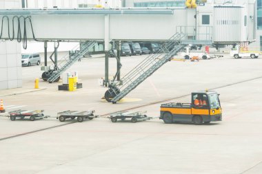 Birkaç boş bagaj vagonu, terminalin arka planında, uçuş çantalarının boşaltılması için uçağa taşınır.