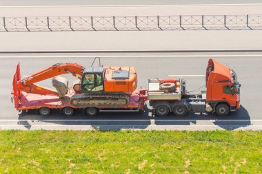 Taşıyıcı kepçe, nakledilmek üzere ağır yük vagonunda. Uzun mesafe ve Nakliye Hizmetleri. Düşük Yataklı Karavana Yükleniyor