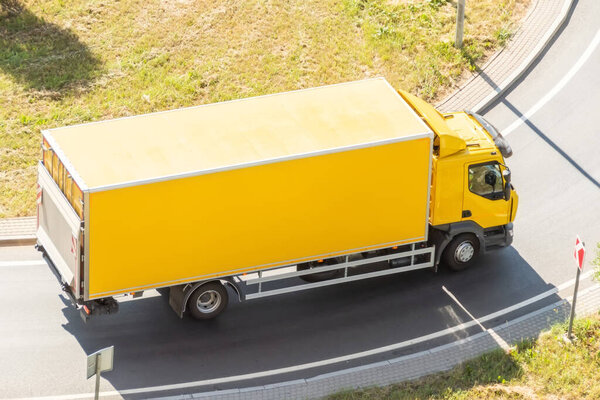 Yellow truck with insulated container box turns on the highway, aerial view