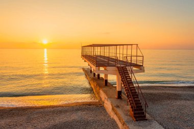 Yaz günbatımında deniz kıyısı ve iskele dalgakıranı, hiç kimse boş kalmaz.